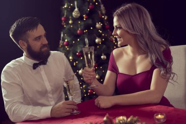 Romantik Noel yemeğinin tadını çıkaran, şampanya içen ve kadeh kaldıran genç ve çekici bir çift. Kıza odaklan.