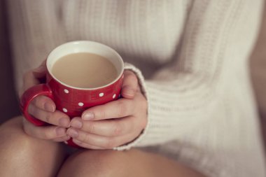 Bir kadının ellerinde bir fincan kahve tutarken beyaz bir kazak giyerken ve boş zamanların tadını çıkarırken.