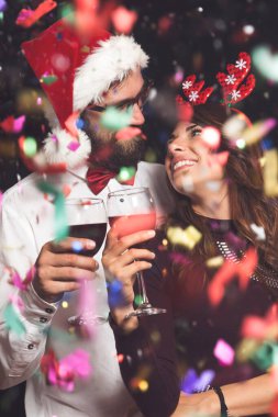Birbirine aşık genç bir çift Noel Baba 'nın şapkasını ve boynuzlarını takıyor, ellerinde şarap kadehleriyle kadeh kaldırıyorlar.
