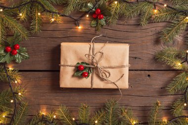 Çam dallarından yapılmış bir çerçeve ve Noel ışıklarından yapılmış güzel paketlenmiş bir hediye kutusu ahşap masaya yerleştirilmiş.