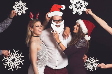 Üç genç arkadaş Noel Baba 'nın şapkalarını takıp, ellerinde karton kar taneleri tutarak ve dans ederek yeni yıl partisinde eğleniyorlar.