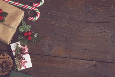 Güzel paketlenmiş Noel hediye kutuları, baston şekerler, çam kozalakları ve tahta bir masada ökseotu manzarası.