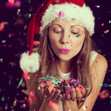 Noel Baba 'nın şapkasını takan güzel genç bir kadın, yılbaşı partisinde eğleniyor, konfetileri uçuruyor ve öpücükler yolluyor.