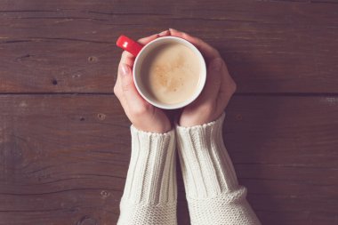 Tahta masada bir fincan kahve tutan bir kadının üst görüntüsü.