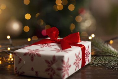 Güzel paketlenmiş bir Noel hediyesinin ve kırsal bir masanın üzerindeki Noel ışıklarının ayrıntıları. Seçici odak