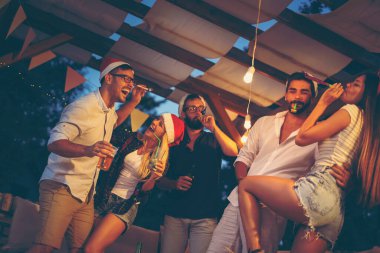 Bir grup genç arkadaş dans ediyor, parti düdüğü çalıyor, içiyor ve dışarıda yeni yıl partisinde eğleniyorlar. Soldaki kıza odaklan.