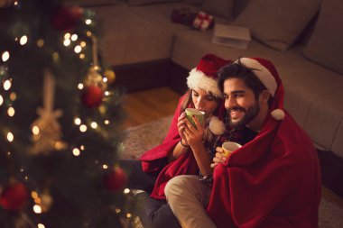 Birbirine aşık bir çift Noel ağacının yanında oturuyor, Noel Baba şapkaları takıyor, sıcak çay içiyor ve hediyelerini değiş tokuş ediyorlar. Kadına odaklan.