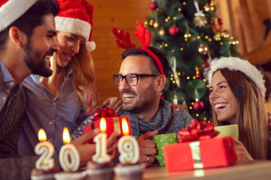 2019 numaralı mumlu kekler, arka planda kutlama ve hediye alışverişi yapan bir grup arkadaşla bir sehpanın üzerine yerleştirilmiş.