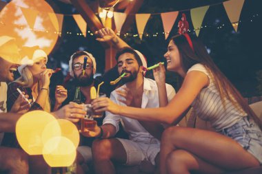 Bir grup genç arkadaş parti düdüğü çalıyor, bira içiyor ve yeni yıl partisinde eğleniyorlar. Sağdaki adama odaklan.