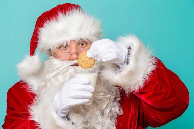 Noel Baba, Noel arifesinde süt içiyor ve kurabiye yiyor. Renkli arka planda izole edilmiş.