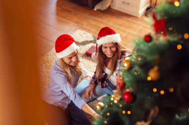 Noel ağacını süsleyen ve Noel sabahı eğlenen iki kız arkadaşın yüksek açılı görüntüsü