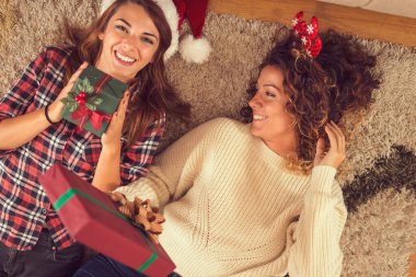 Oturma odasının zemininde iki güzel kadının güzel paketlenmiş Noel hediye kutularını tutarken görüntüsü. Sağdaki kıza odaklan.