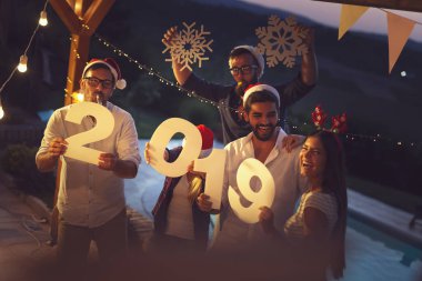 Bir grup genç arkadaş yeni yıl havuz partisinde eğleniyorlar, dans ediyorlar ve karton kar taneleri tutuyorlar ve 2019 numara. Rakamları tutan adamlara odaklan.