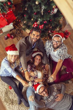Bir grup arkadaşın güzel dekore edilmiş bir Noel ağacının yanında oturup şampanya kadehleriyle kadeh kaldırdığı en iyi manzara.