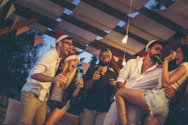 Bir grup genç arkadaş dans ediyor, parti düdüğü çalıyor, içiyor ve yeni yıl partisinde eğleniyorlar.