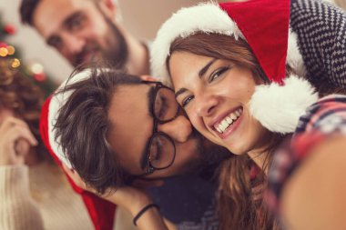 Güzel bir Noel ağacının yanında oturan, Noel günü sarılan, öpüşen ve eğlenen güzel bir çift.