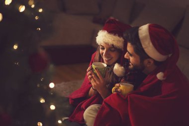 Birbirine aşık bir çift Noel ağacının yanında oturuyor, Noel Baba 'nın şapkalarını takıyor, sıcak çay içiyor ve birlikte romantik anların tadını çıkarıyor. Kıza odaklan.