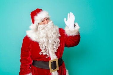 Noel Baba kameraya el sallıyor, yeni yılı kutluyor ve eğleniyor. Renkli arka planda izole bir şekilde.