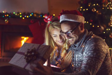 Aşık genç bir çift şöminenin yanında oturuyor ve güzel dekore edilmiş bir Noel ağacı, hediyeleri açıyor ve Noel arifesinde eğleniyorlar. Kıza odaklan.