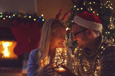 Birbirlerine aşık genç bir çift şöminenin yanında oturmuş Noel ağacını süslüyor ve Noel büyüsünün tadını çıkarıyorlar.