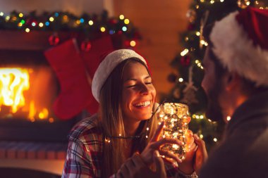 Birbirlerine aşık genç bir çift şöminenin yanında oturmuş Noel ağacını süslüyor ve Noel büyüsünün tadını çıkarıyorlar.