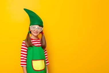 Küçük güzel bir kızın portresi Noel elf kostümü giymiş ve sarı renkli arka planda parti gözlüğü takmış fotokopi alanı olan.