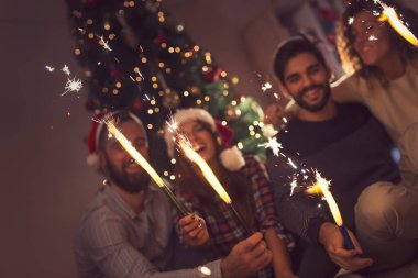 Bir grup genç arkadaş yılbaşı kutlamasında eğleniyorlar, gece yarısı geri sayımında maytap tutuyorlar. Maytaplara odaklan.