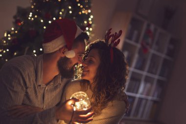 Güzel bir çift Noel ağacının yanında, oturma odasında oturmuş Noel ışıklarıyla dolu bir kavanozu tutuyorlar.