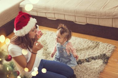 Anne ve kızı güzel dekore edilmiş bir Noel ağacının yanında yerde oynuyorlar, kabarcıklar yapıyorlar.