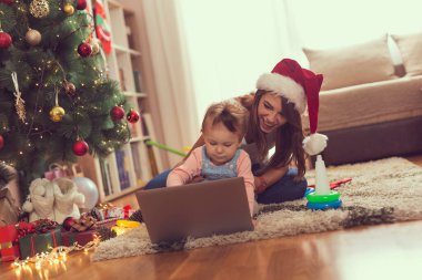 Anne ve kızı bir Noel ağacının yanında oturmuş dizüstü bilgisayarda çizgi film izliyor ve eğleniyorlar. Annesine odaklan.