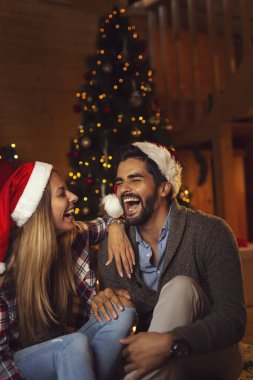 Birbirine aşık bir çift Noel Baba şapkası takıyor şöminenin yanında oturuyor ve Noel ağacını süslüyor, Noel arifesinde eğleniyorlar. Adama odaklan.