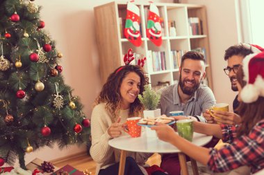 Bir grup arkadaş bir Noel ağacının yanında oturuyor, Noel kurabiyeleri yiyor, kahve içiyor ve eğleniyorlar. Boynuzlu kıza odaklan.