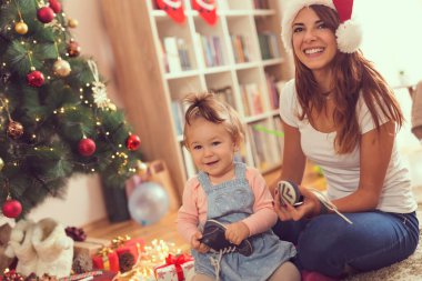 Güzel, genç bir anne ve kız Noel ağacının yanında oturup Noel sabahı eğleniyorlar.