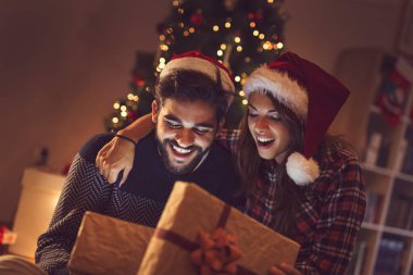 Birbirine aşık genç bir çift Noel ağacının yanında oturuyor, hediyeleri açıyor ve eğleniyorlar.