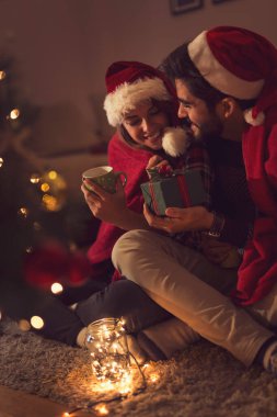 Birbirine aşık bir çift Noel ağacının yanında oturuyor, Noel Baba 'nın şapkalarını takıyor, sıcak çay içiyor ve hediyelerini değiş tokuş ediyorlar. Adama odaklan.