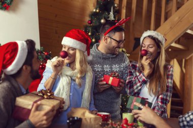 Güzel dekore edilmiş bir Noel ağacının yanında oturan bir grup genç arkadaş, Noel hediyelerini değiş tokuş edip eğleniyorlar. Ortadaki çifte odaklan.