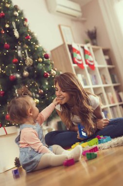 Güzel, genç bir anne ve kız Noel ağacının yanında oturup Noel sabahı eğleniyorlar.