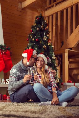 Aşık, Noel Baba şapkaları giyen, güzel bir şekilde dekore edilmiş bir Noel ağacı yanında oturan ve bardak şampanya ile bir tost yapmak güzel çift