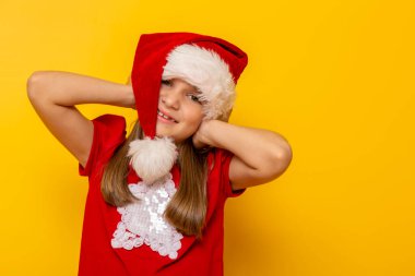 Noel Baba şapkası takan çocuk iki eliyle kulaklarını kapatıyor, dinlemiyor, sarı renkli arka planda izole edilmiş ve kopya alanı olan.