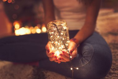 Noel ışıklarıyla dolu bir kavanozu tutan bir kadının eli. Seçici odak