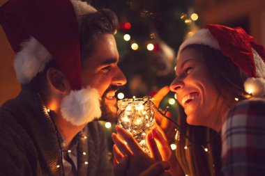 Aşık genç bir çift şöminenin yanında oturuyor ve Noel ağacını süslüyor, Noel büyüsünün tadını çıkarıyorlar. Adama odaklan.