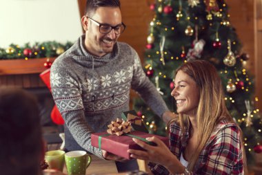 Güzel bir Noel ağacının yanında oturan, birbirlerine Noel hediyelerini veren ve Noel sabahı eğlenen genç ve güzel bir çift.