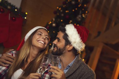 Birbirine aşık güzel bir çift, Noel Baba şapkası takıyorlar, güzel dekore edilmiş bir Noel ağacının yanında oturuyorlar ve şampanya kadehleriyle kadeh kaldırıyorlar. Kıza odaklan.