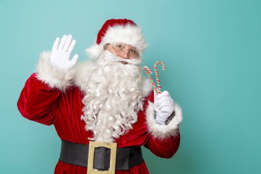 Noel Baba elinde baston şekerler ve kameraya el sallıyor. Nane rengi arka planda izole edilmiş.