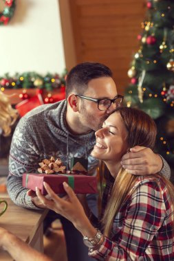 Güzel dekore edilmiş Noel ağacının yanında oturan, sarılan, öpüşen, Noel hediyelerini veren ve eğlenen çift.