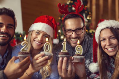 Bir grup genç arkadaş Noel 'i kutluyorlar, ellerinde 2019 numaralı mumlarla kek tutuyorlar. Ortadaki kıza odaklan.