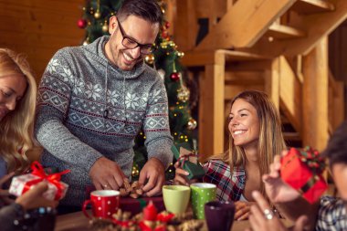 Güzel dekore edilmiş bir Noel ağacının yanında oturan bir grup genç arkadaş, Noel hediyelerini değiş tokuş edip eğleniyorlar.