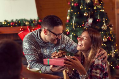 Güzel dekore edilmiş bir Noel ağacının yanında oturan bir grup genç arkadaş, Noel hediyelerini değiş tokuş ediyorlar.