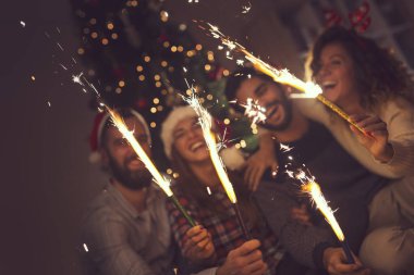 Bir grup genç arkadaş yılbaşı kutlamasında eğleniyorlar, gece yarısı geri sayımında maytap tutuyorlar. Maytaplara odaklan.