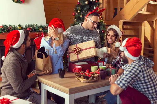 Güzel dekore edilmiş bir Noel ağacının yanında oturan bir grup genç arkadaş Noel hediyelerini açıyor, kahve içiyor ve eğleniyorlar.